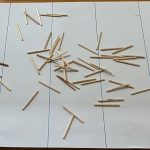 A photo of a sheet of paper with equally spaced lines marked on it. A number of matchsticks have been dropped on the paper.
